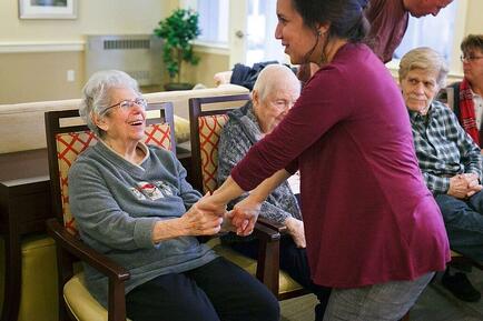 older woman sitting smiling while younger woman holds her hands