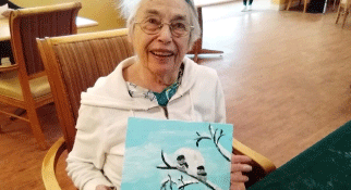 older woman sitting and holding up a picture she painted