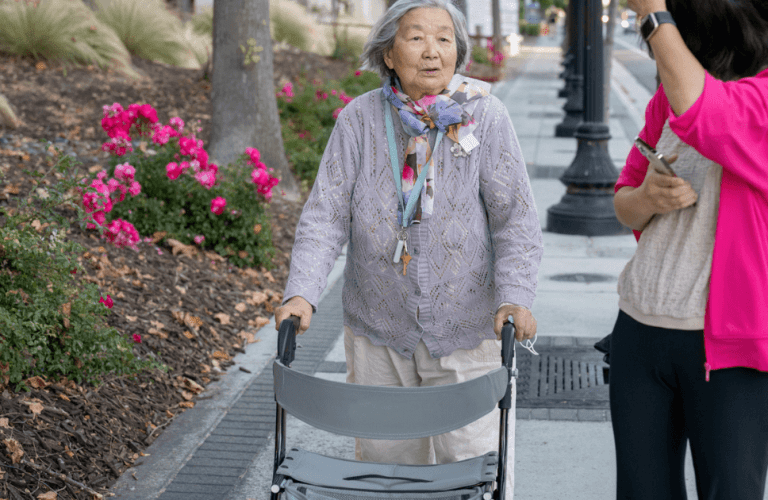 Adult woman walking outdoors with senior woman using a walker.
