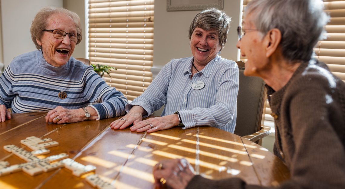 three elderly women smiling while playing dominoes