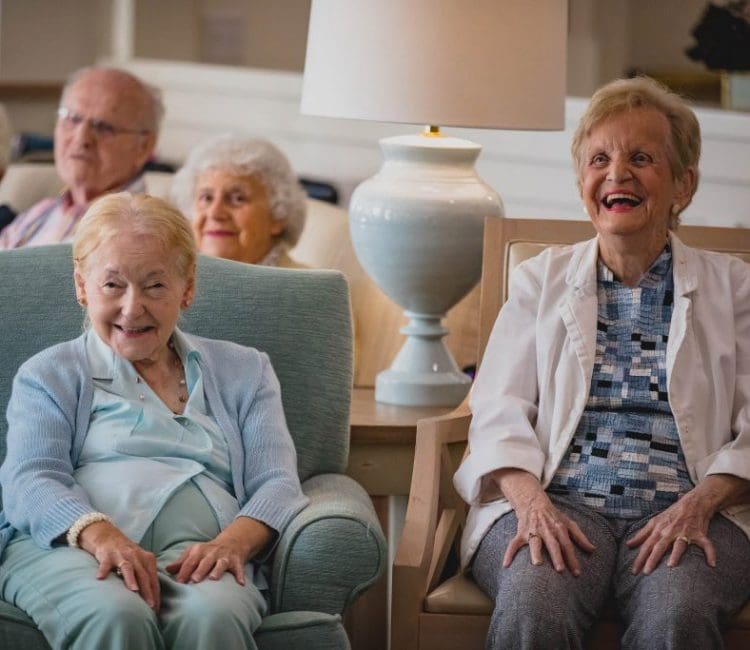 two woman residents sitting and smiling together with other residents in the background