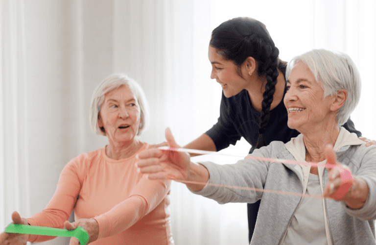 Two older woman that are memory care residents exercising with caregiver.