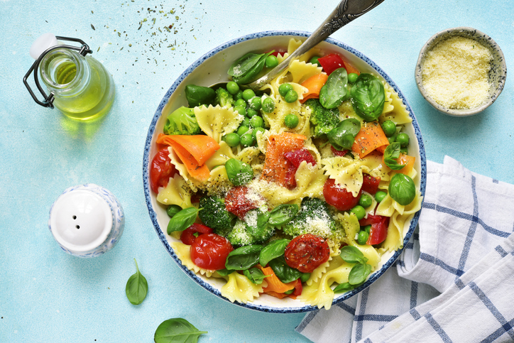 Pasta primavera with spring vegetables in a white vintage bowl on a light blue slate, stone or concrete background.Top view.