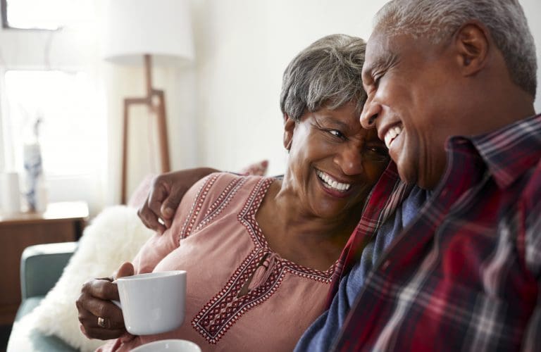 Loving Senior with Spouse Sitting On Sofa At Home Relaxing With Hot Drink