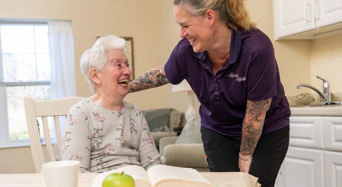 Resident reading at the kitchen table, while laughing with one of the Northbridge staff members