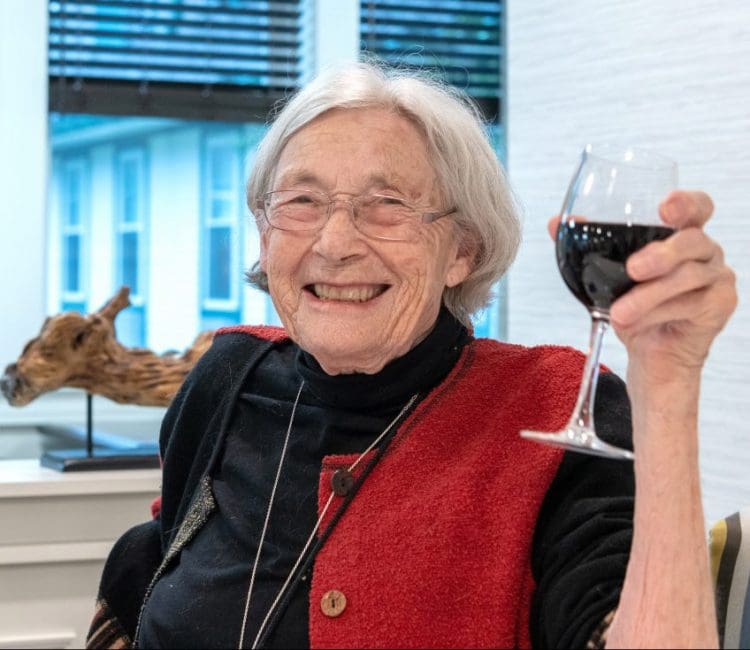 a resident, smiling older woman holding a wine glass